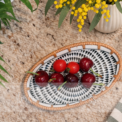 Natural woven rattan edge beautifully surrounding the intricate black spiral and teardrop ceramic artwork.
