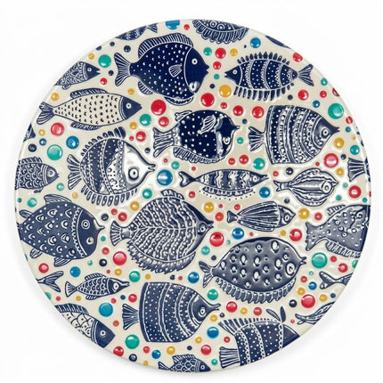 A round ceramic coaster featuring intricate navy blue fish, colourful dots and playful folk-art details on a warm cream background.