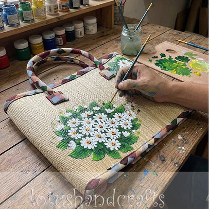 Handwoven seagrass tote bag with artistic painted daisy design.