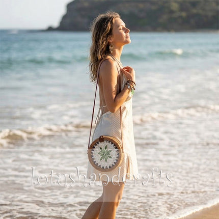 A round rattan crossbody bag with mother of pearl leaf mosaic and leather strap elevates style.