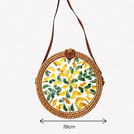 Round rattan crossbody bag featuring a green and yellow mother of pearl leaf inlay, size.