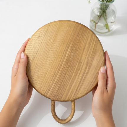 Round wood cutting board with loop handle crafted from durable natural Ashwood.